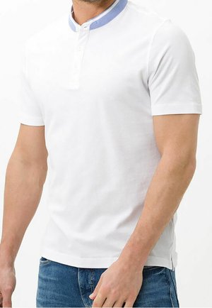 Homme portant un t-shirt henley à manches courtes blanc avec un détail de col bleu et un jean bleu, debout devant un fond blanc uni.