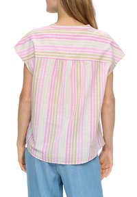 Frau in einer lockeren kurzärmeligen Bluse mit vertikalen rosa, beige und weißen Streifen, kombiniert mit hellblauen Jeans.