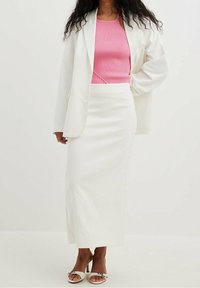 Witte blazer over een roze geribd tanktop, gecombineerd met een witte kokerrok en witte sandaalhakken met bandjes; gladde textuur en aansluitend ontwerp.