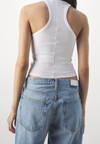 Canotta bianca a costine con una silhouette aderente, abbinata a jeans azzurri a vita alta con tasche posteriori prominenti e un lavaggio chiaro.