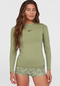 Langärmeliger grüner Rashguard mit schwarzem Logo, kombiniert mit gemusterten grünen Shorts mit weißen Akzenten und einem strukturierten Design.