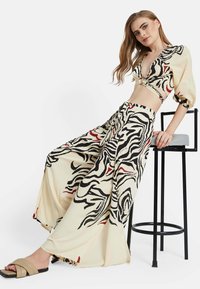 Conjunto de dos piezas que incluye un top corto y pantalones de pierna ancha en una tela crema con patrones abstractos en negro y rojo.