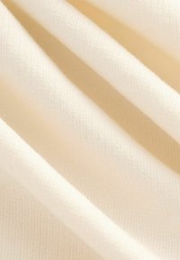 Tecido color crema, suavemente texturizado con un fino tricot. La drapeado muestra pliegues suaves, destacando su ligereza y calidad suave.