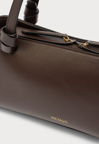 Σκουρόχρωμη καφέ δερμάτινη τσάντα χειρός με χρυσλό φερμουάρ και μικρό χρυσό λογότυπο Neous κοντά στην κάτω άκρη.