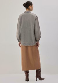 Siva prevelika jakna z napihnjenimi rokavi, kombinirana z rebrasto bež krilo in rjavimi škornji do kolen, videno od zadaj.
