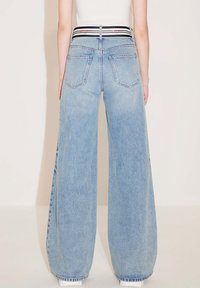 Jeans de pierna ancha de color azul claro con un cinturón a rayas en blanco y negro, que cuentan con bolsillos traseros y una textura de denim desgastado.