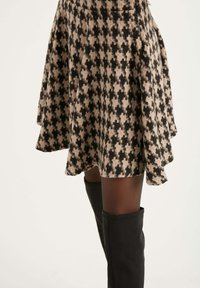 Černá a béžová sukně s houndstooth vzorem ve splývavém designu, vyrobená z texturované látky, spárovaná s černými vysokými kozačkami.