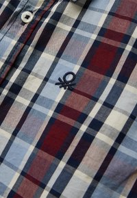 Camicia di cotone a quadri nei colori blu, rosso e crema. Presenta un colletto con bottoni e un logo ricamato sul petto.