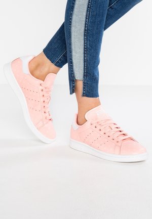 Zapatillas deportivas rosa claro con detalles blancos usadas con vaqueros cortos bicolor azul sobre un fondo claro y liso.
