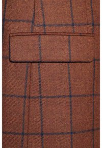 Brązowa tkanina w kratkę z niebieskimi liniami, z kieszenią na klapę. Tekstura jest tkana, prezentując uporządkowany wzór i bogatą kolorystykę.