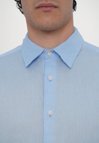 Chemise boutonnière bleu clair avec col classique, en tissu léger avec une texture subtile et boutons blancs.