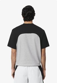 Camiseta de mangas cortas con parte superior negra y parte inferior trasera gris, con cuello redondo y un corte relajado. Fabricada en una suave mezcla de algodón.