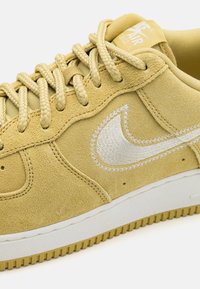 Yellow suede sneaker with white embroidered branding and textured laces, featuring a contrasting white rubber sole and light cushioning.