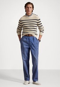 Beige randig stickad tröja med rund hals; ljusblå plisserade byxor; brunt läderbälte; vita sneakers. Inga särskilda detaljer eller mönster.