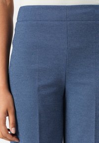 Blaue gemusterte Hosen mit glatter Textur, schlankem Schnitt und einem Bund, der sichtbare Nähte und dezente Punktmuster aufweist.