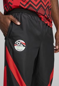 Sorteidrettsprosedyrer med røde sideakenter, med en logo-lapp for Det egyptiske fotballforbundet på venstre lår. Glatt tekstur.