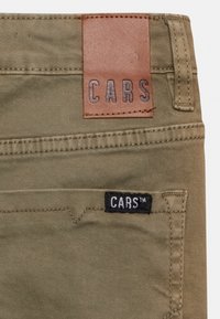 Olijfgroene katoenen broeken met een bruine leren patch waarop "CARS" staat en een zwarte tag met "CARS™" op de achterzak.