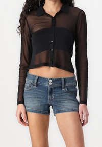 Svart genomskinlig långärmad cropped skjorta med knäppning fram och krage, parat med blå denimshorts med tvåknapps stängning och fickor.