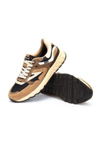 Zapatillas con parte superior de ante marrón, paneles de malla negra, acentos en crema y una suela gruesa. Presenta un dibujo de textura en la suela y una marca prominente.