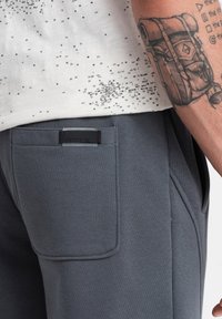 Grå sweatpants lavet af blødt stof med fremtrædende sidelommer og et mærketag på bagsiden. T-shirten har et tekstureret print.