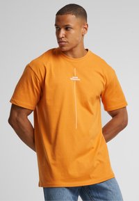 Oransje bomull t-skjorte med rund hals, korte ermer og et hvitt grafisk tekstdesign som sier "tenk annerledes" på fronten.