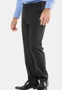Zwarte formele broek met een recht model. Gemaakt van gladde stof, met riemlussen, en gedragen met zwarte dresschoenen.
