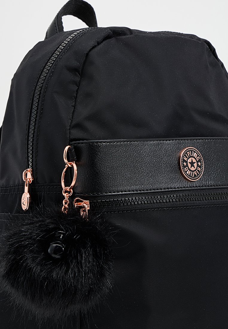 Zaino in nylon nero con un accento in pelle, dotato di un logo rotondo, chiusura con zip e un portachiavi a pompon in pelliccia nera staccabile.