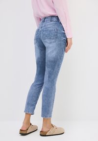 Jeans en denim bleu clair avec une coupe skinny, dotés d'une taille haute, de deux poches arrière et d'une finition décolorée. Associés à des sabots beiges.