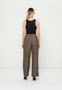 Ruske leve bukse med elastisk midje og to baklommer, kombinert med en tettsittende svart tanktop. Stoffet har en glatt tekstur.