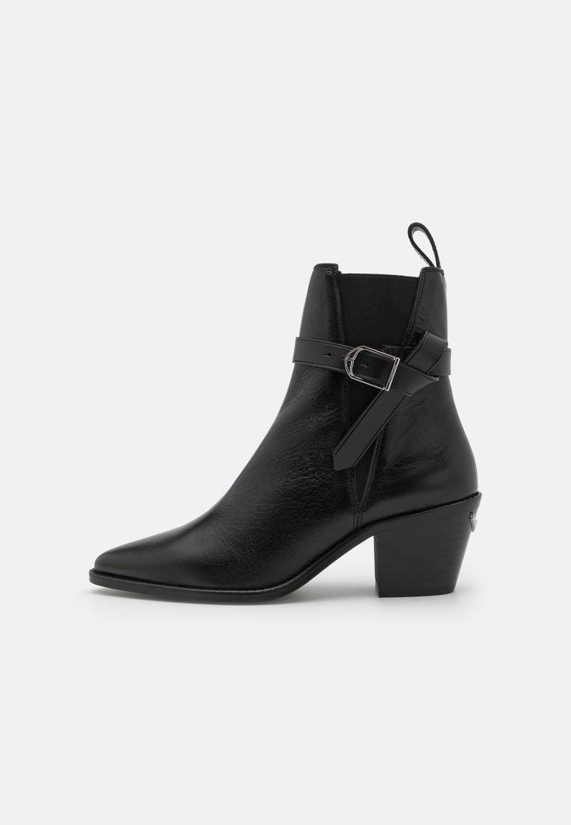 Botte de cheville en cuir noir avec bout pointu, talon bloc et détail de boucle sur le côté. Présente une texture lisse et une languette à l'arrière.