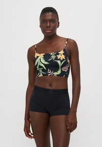 Černý květinový crop top s tenkými ramínky, zdobený žlutými a zelenými květinovými vzory. V kombinaci s černými šortkami s vysokým pasem a logem.