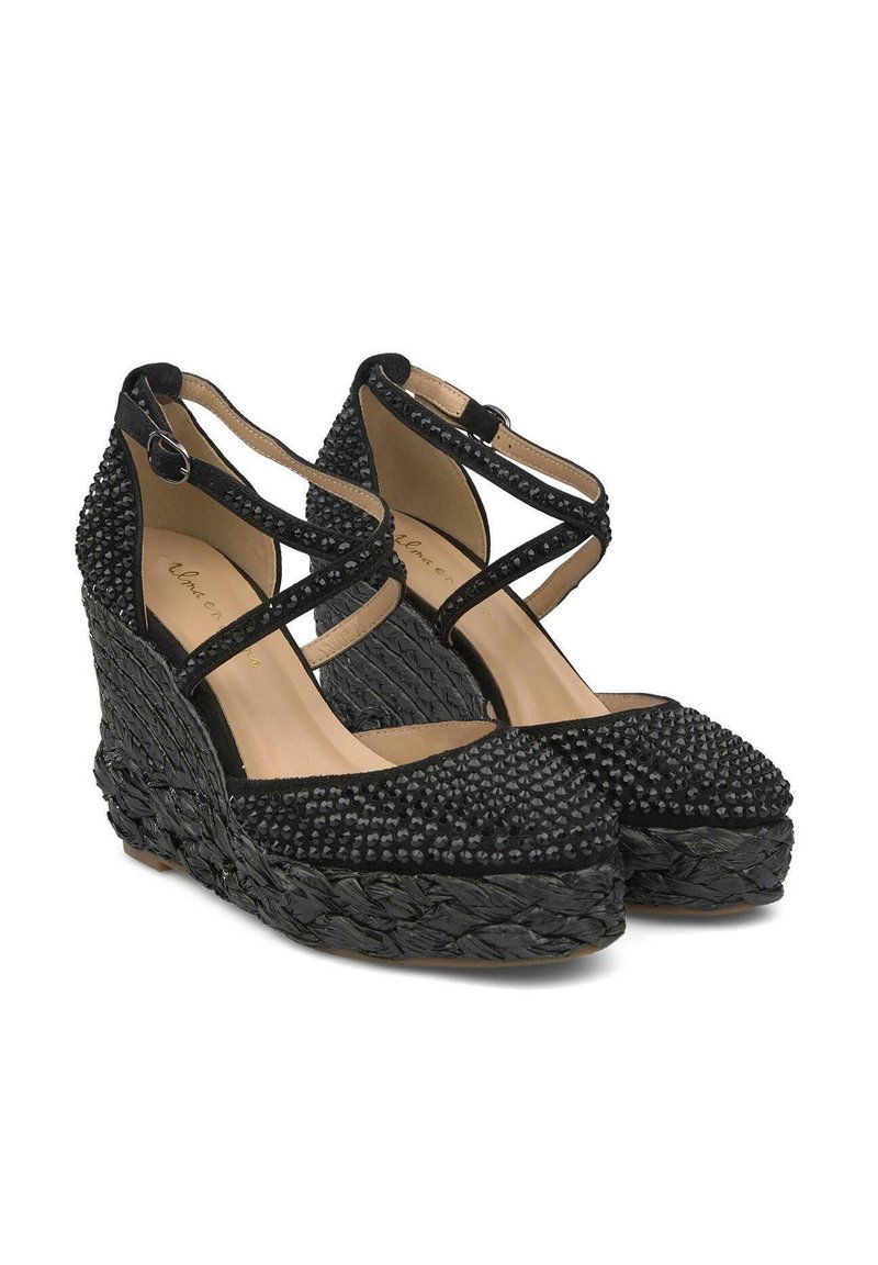 Sandalias de cuña negras con tela texturizada, adornadas con tachuelas negras, que presentan correas de tobillo entrelazadas y una base tejida.