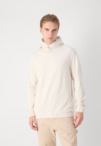 Sudadera de color beige claro con canalé, con cuello alto y un bolsillo tipo canguro. Mangas largas con puños ajustados, hecha de un material suave.