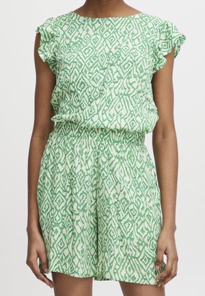 Ärmelloser grüner und weiß gemusterter Jumpsuit mit gerafften Schultern und einem elastischen Bund, getragen von einer stehenden Person.