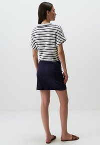 Top a righe, maniche corte, di colore crema e blu navy, abbinato a una minigonna blu navy. Tessuto liscio, vestibilità casual con strisce orizzontali. Sandali piatti marroni.