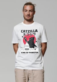Witte katoen T-shirt met een grafisch ontwerp van een zwarte kat tegen een rode cirkel, met de tekst "CATZILLA" en "KING OF PAWSTER" eronder.