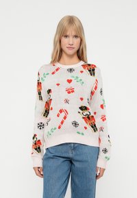 Pullover mit einem hellrosa Hintergrund, verziert mit festlichen Motiven wie einem Nussknacker, Zuckerstangen, Geschenken und Herzen. Hergestellt aus weichem, gewebtem Material.