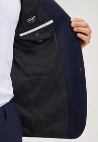 Giacca da abito blu navy che mostra la fodera interna con un motivo sottile, tasca ed etichetta del marchio. Design slim fit con dettagli di cuciture sartoriali.