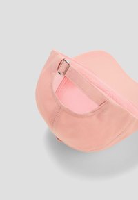 Roze pet van zacht textiel met een afgeronde vorm. Voorzien van een zilverkleurige metalen verstelklem en een gladde, textuurachtige binnenvoering.