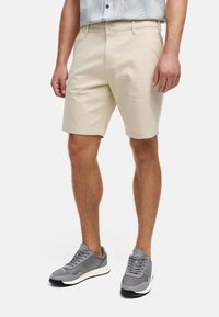 Beige shorts med en almindelig pasform, lavet af blødt stof, med forlommer og knaplukning, parret med grå sportsko.