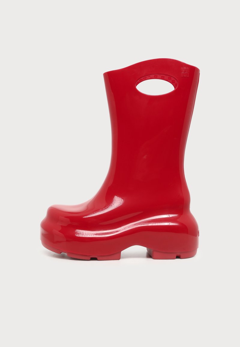 Botte de pluie brillante rouge vif avec une semelle large et un trou de poignée intégré près du haut pour un transport facile.
