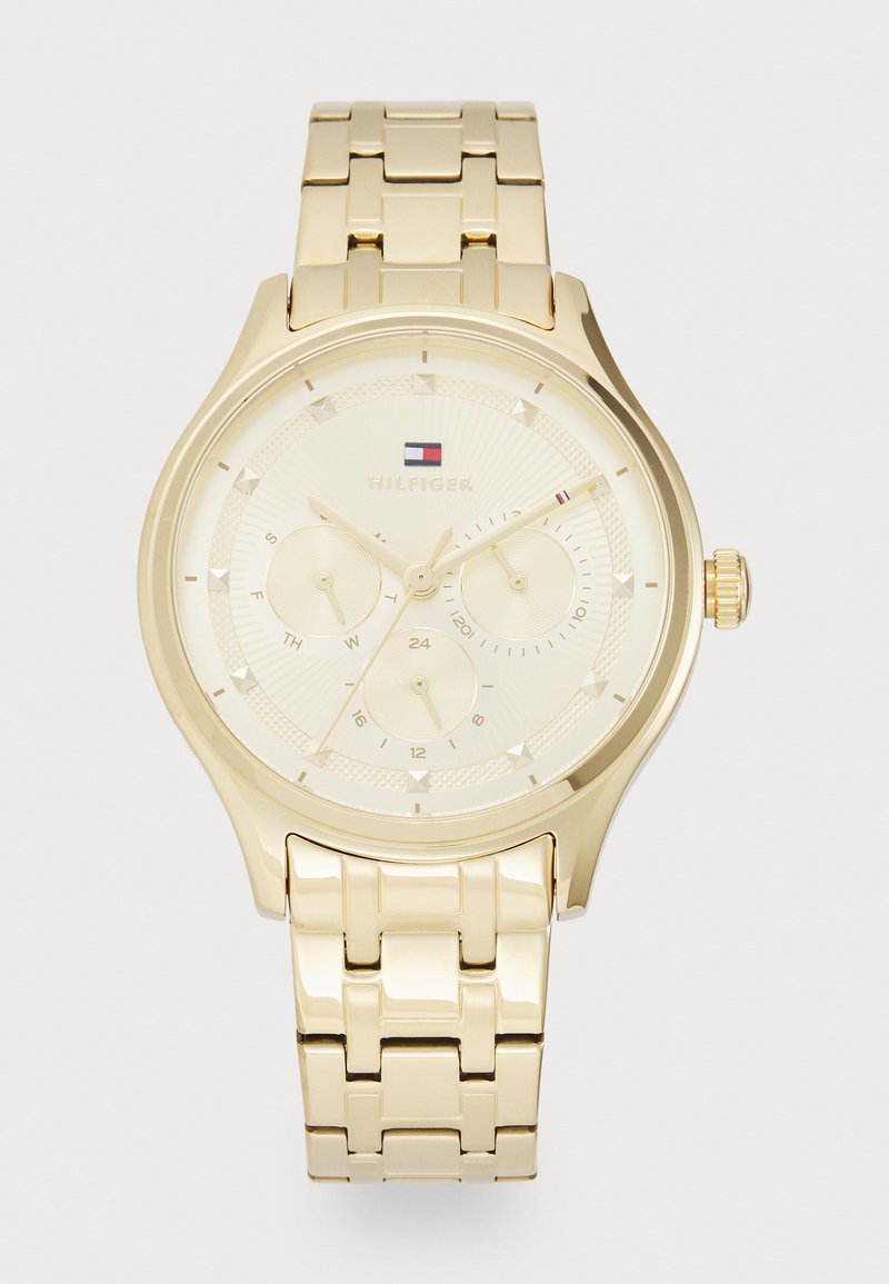 Montre bracelet dorée avec un cadran texturé, des sous-cadrans pour le jour et la date, et un bracelet en maillons métalliques. Boîtier circulaire avec des index proéminents et une couronne.