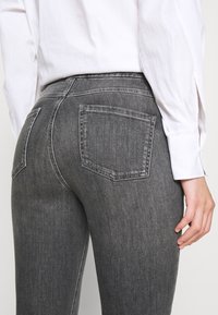 Gray denim jeans with a fitted design, featuring a mid-rise waist and two back pockets. Textured fabric with subtle fading details.