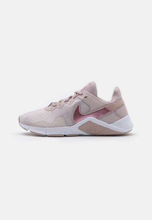 Jasnoróżowy sportowy but Nike z białą podeszwą, różowym logo swoosh, sznurowaniem z przodu i niskim krojem, ukazany z profilu na białym tle.