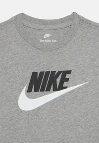 Pilkas medvilninis marškinėliai su apvaliu kaklu, ant jų yra ryškus juodas "NIKE" užrašas ir baltas swoosh logotipas per priekinę dalį.