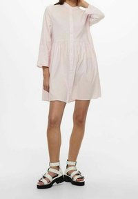 Różowo-biała, paskowana sukienka koszulowa z długimi rękawami, ściągnięta w pasie, z kołnierzykiem. Połączona z białymi sandałami na paski.