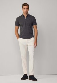 Polo grigio con colletto a zip, abbinato a pantaloni color crema. Il modello indossa scarpe in suede blu navy, con un design minimalista.