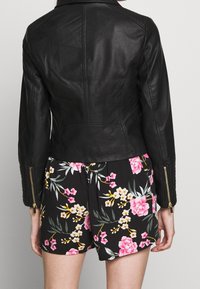 Giacca in pelle nera con un design aderente, spalle imbottite, polsini con zip e dettagli delle tasche piatte. Abbinata a pantaloni corti con motivo floreale.