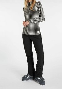 Top a maniche lunghe con motivo houndstooth in bianco e nero, con spalle arricciate, abbinato a pantaloni da sci neri e stivali da sci grigi.