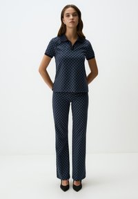Marineblauwe polo met kraag en geometrisch patroon, gecombineerd met bijpassende broeken met hetzelfde patroon. Beide hebben een zachte textuur en een getailleerd ontwerp.